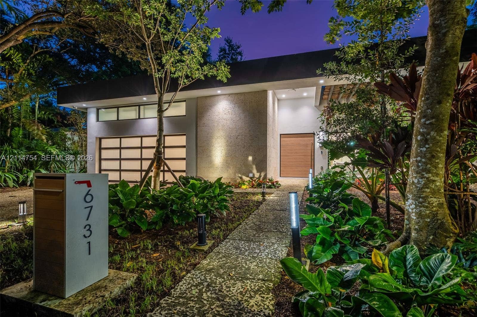 6731 SW 64th Avenue, South Miami, FL 33143 Contemporary exterior featuring a textured stone facade, a multi-pane frosted glass garage door, clerestory windows, and a pergola-covered entry