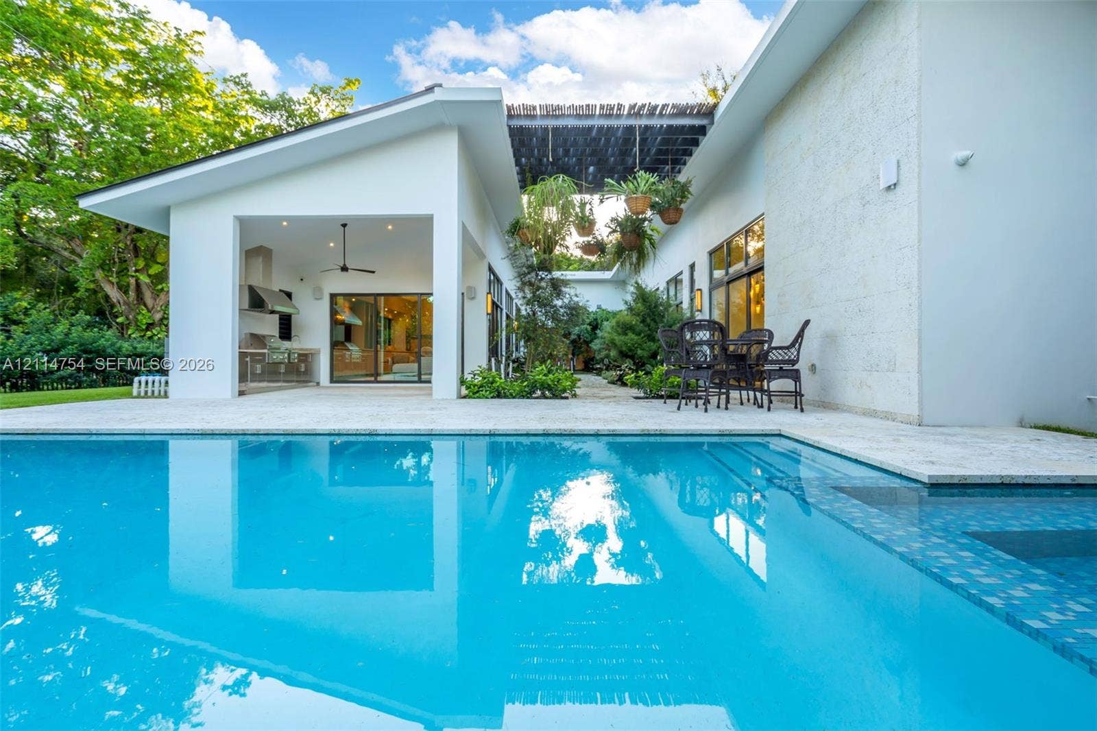 6731 SW 64th Avenue, South Miami, FL 33143 In-ground swimming pool with tiled border, expansive stone-paved patio, covered outdoor kitchen with stainless steel appliances, and minimalist white exterior siding