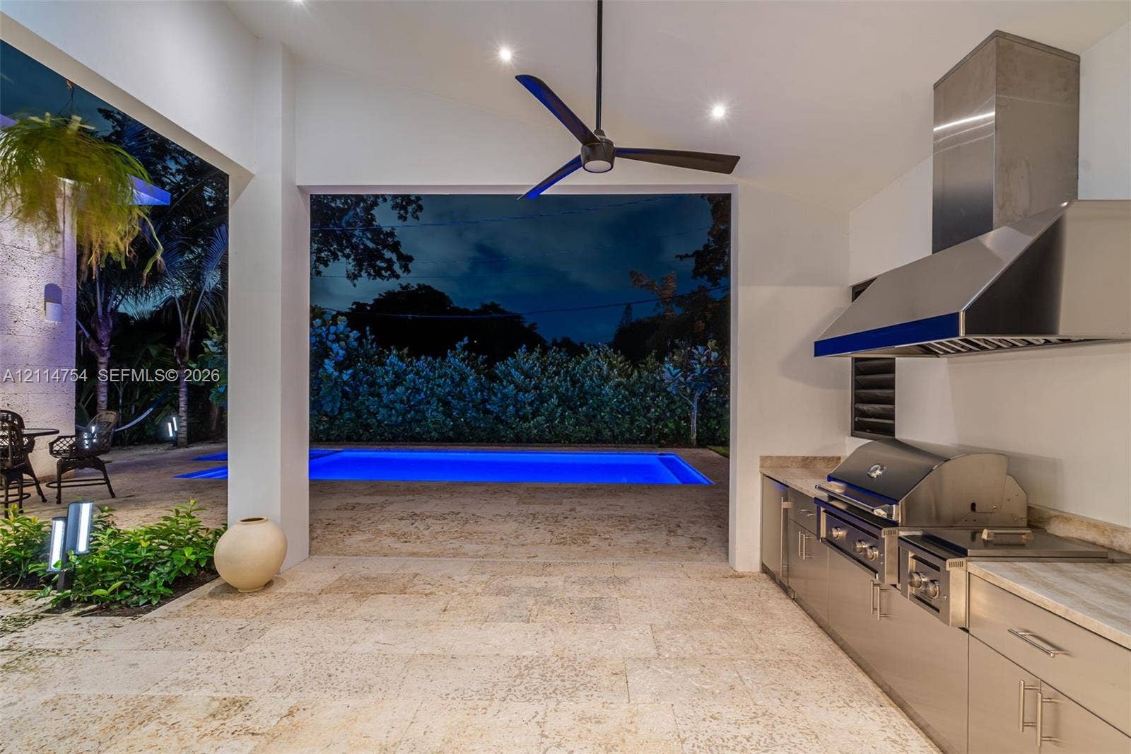 6731 SW 64th Avenue, South Miami, FL 33143 Modern contemporary facade featuring a textured stone accent wall, natural wood-finish front door, horizontal-pane garage door, overhead beam detailing, and clerestory windows