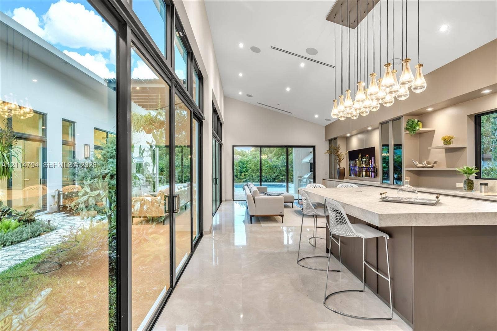 6731 SW 64th Avenue, South Miami, FL 33143 Vaulted ceilings with recessed lighting, full-height glass sliding doors, large-scale crystal and metal chandelier, built-in cabinetry with natural stone countertop, and polished tile flooring