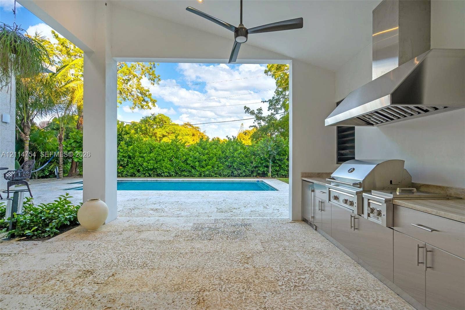 6731 SW 64th Avenue, South Miami, FL 33143 Covered patio featuring stone tile flooring, stainless steel outdoor kitchen with built-in grill, stone countertop, ceiling fan, and expansive sliding glass doors