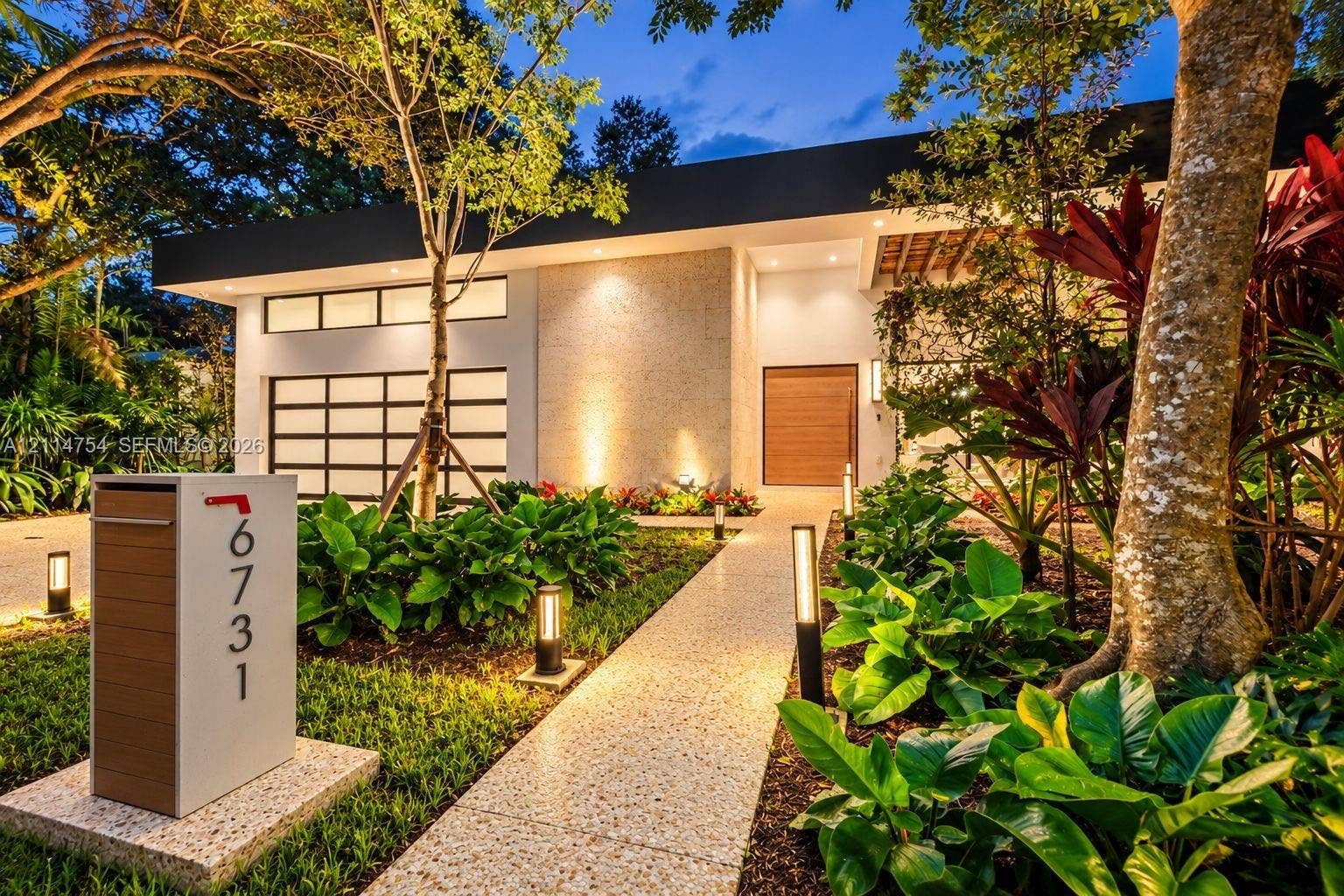 6731 SW 64th Avenue, South Miami, FL 33143 Pivot entry door featuring a light-toned wood finish and a long cylindrical metal handle, textured stone exterior wall, vertical wall-mounted exterior light fixture, and polished stone tile flooring