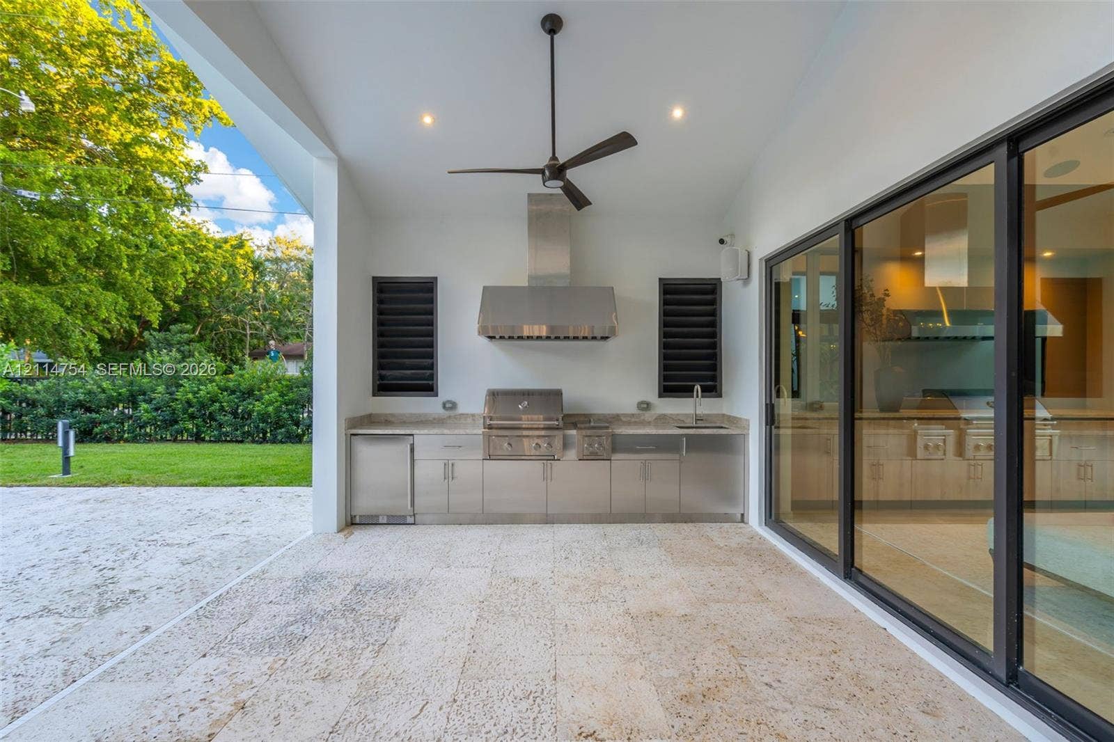 6731 SW 64th Avenue, South Miami, FL 33143 Covered patio featuring stone tile flooring, stainless steel outdoor kitchen with built-in grill, stone countertop, ceiling fan, and expansive sliding glass doors