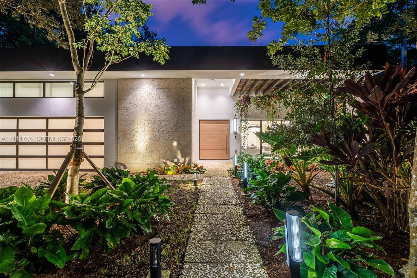 6731 SW 64th Avenue, South Miami, FL 33143 Modern exterior featuring a flat roofline, clerestory windows, a multi-panel glass garage door, a natural wood entry door, and a stone-paver walkway