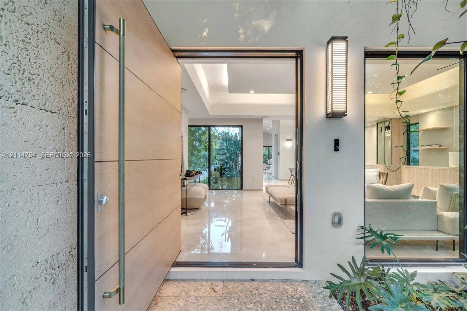 6731 SW 64th Avenue, South Miami, FL 33143 Tray ceiling with cove lighting, expansive floor-to-ceiling glass paneling, polished stone flooring, custom built-in cabinetry with floating shelving, and large-format wood-finish entry door
