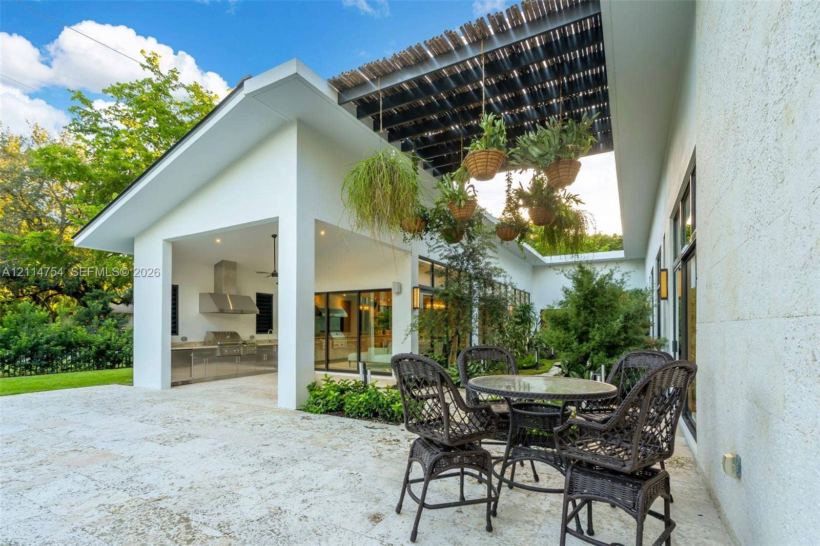 6731 SW 64th Avenue, South Miami, FL 33143 In-ground swimming pool with tiled border, expansive stone-paved patio, covered outdoor kitchen with stainless steel appliances, and minimalist white exterior siding