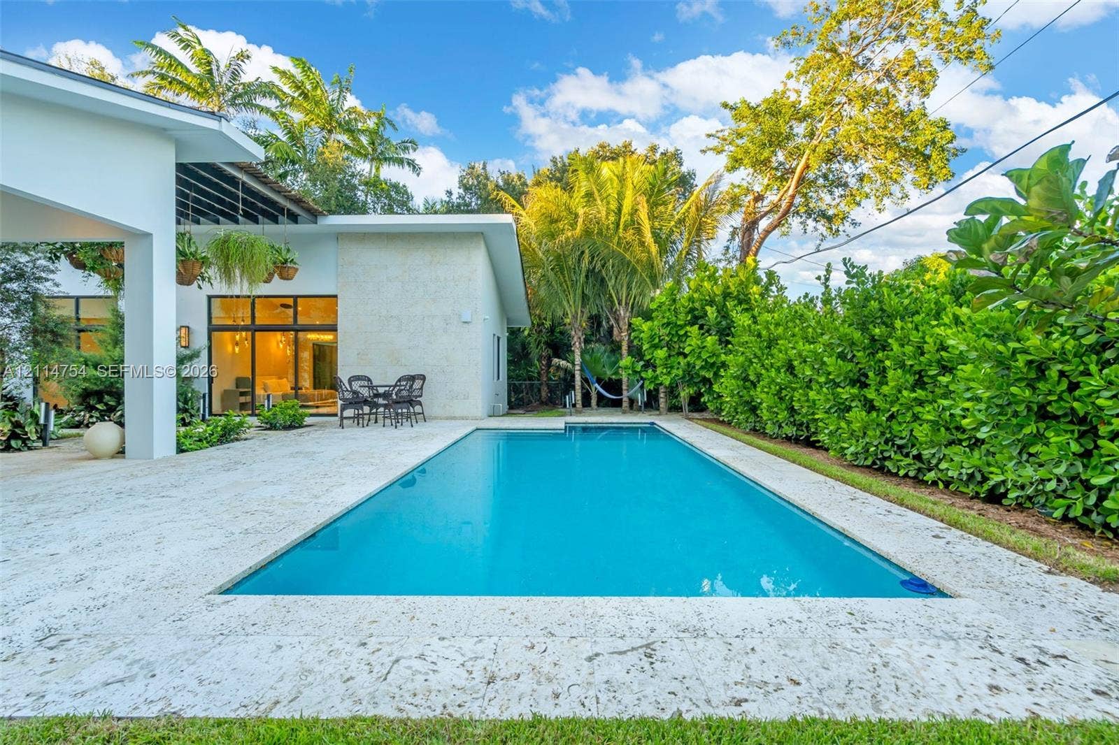 6731 SW 64th Avenue, South Miami, FL 33143 Covered patio featuring stone-tiled flooring, a built-in outdoor kitchen with stainless steel appliances, a slatted overhead architectural structure, and floor-to-ceiling glass sliding doors