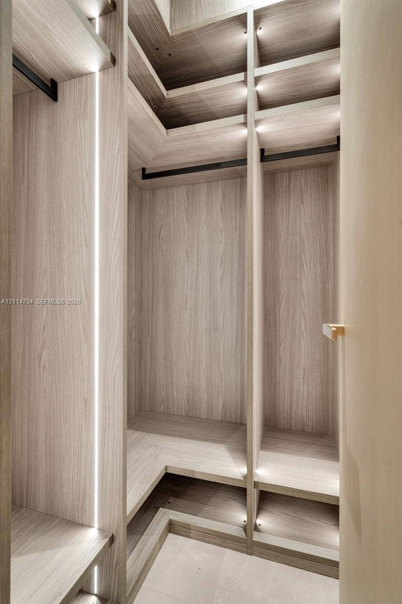6731 SW 64th Avenue, South Miami, FL 33143 Walk-in shower with vertical stone-finish tiling, brass-toned rainfall shower head, wall-mounted vanity with integrated sink, and illuminated mirrored medicine cabinet
