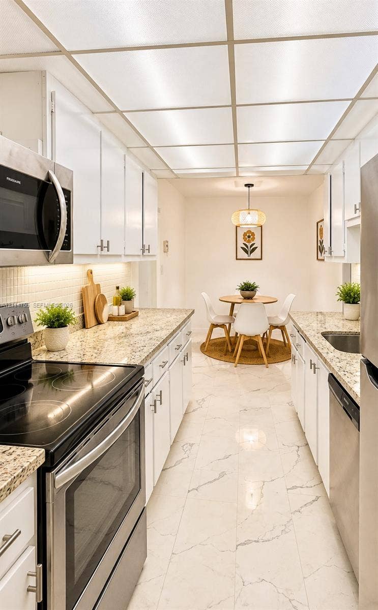 231 174th Street, #MO-3, Sunny Isles Beach, FL 33160 Kitchen featuring stone countertops, stainless steel appliances, white cabinetry with silver-tone hardware, and large-format tile flooring