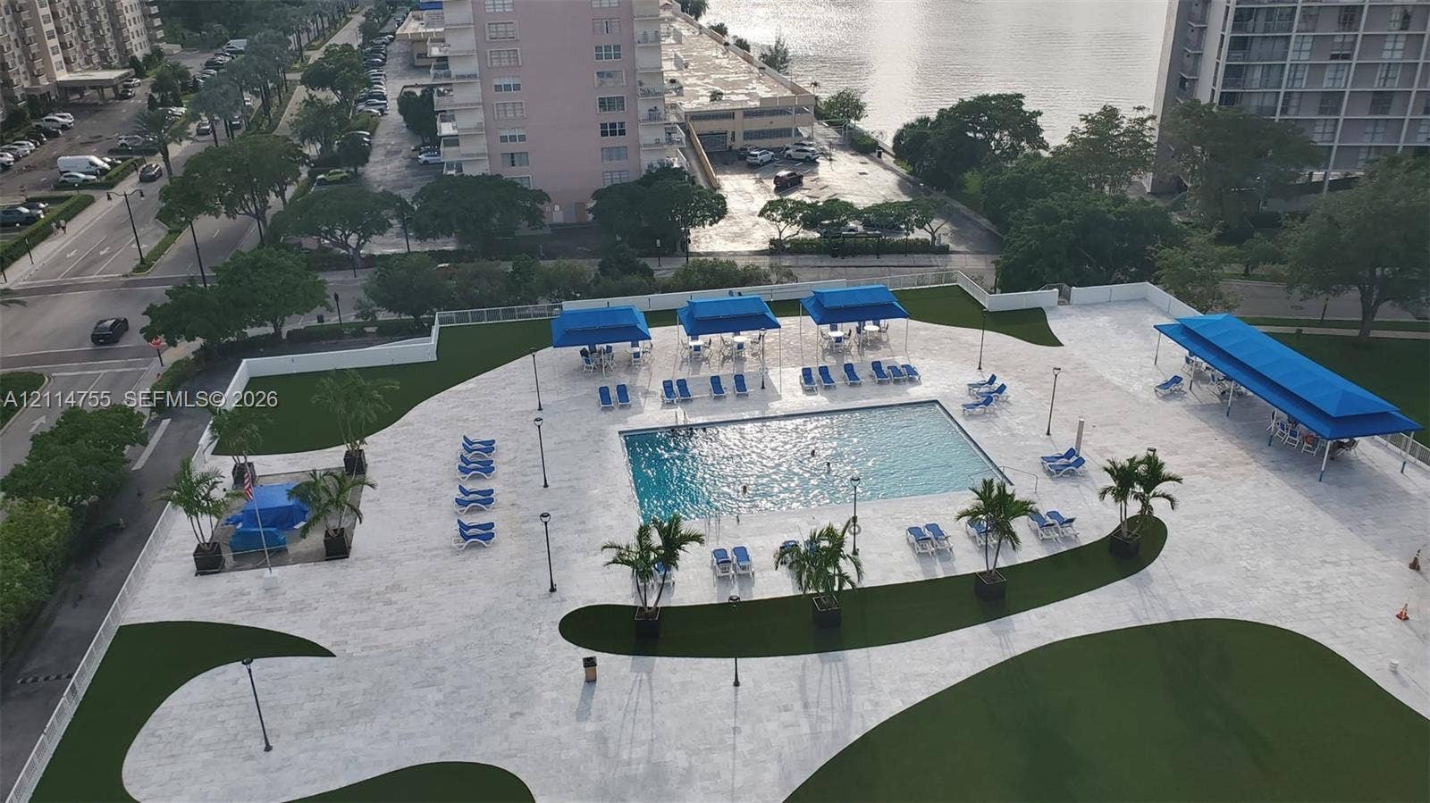 231 174th Street, #MO-3, Sunny Isles Beach, FL 33160 Outdoor terrace featuring a swimming pool, stone-finish decking, multiple blue-canopied structures, manicured green space, and perimeter lighting