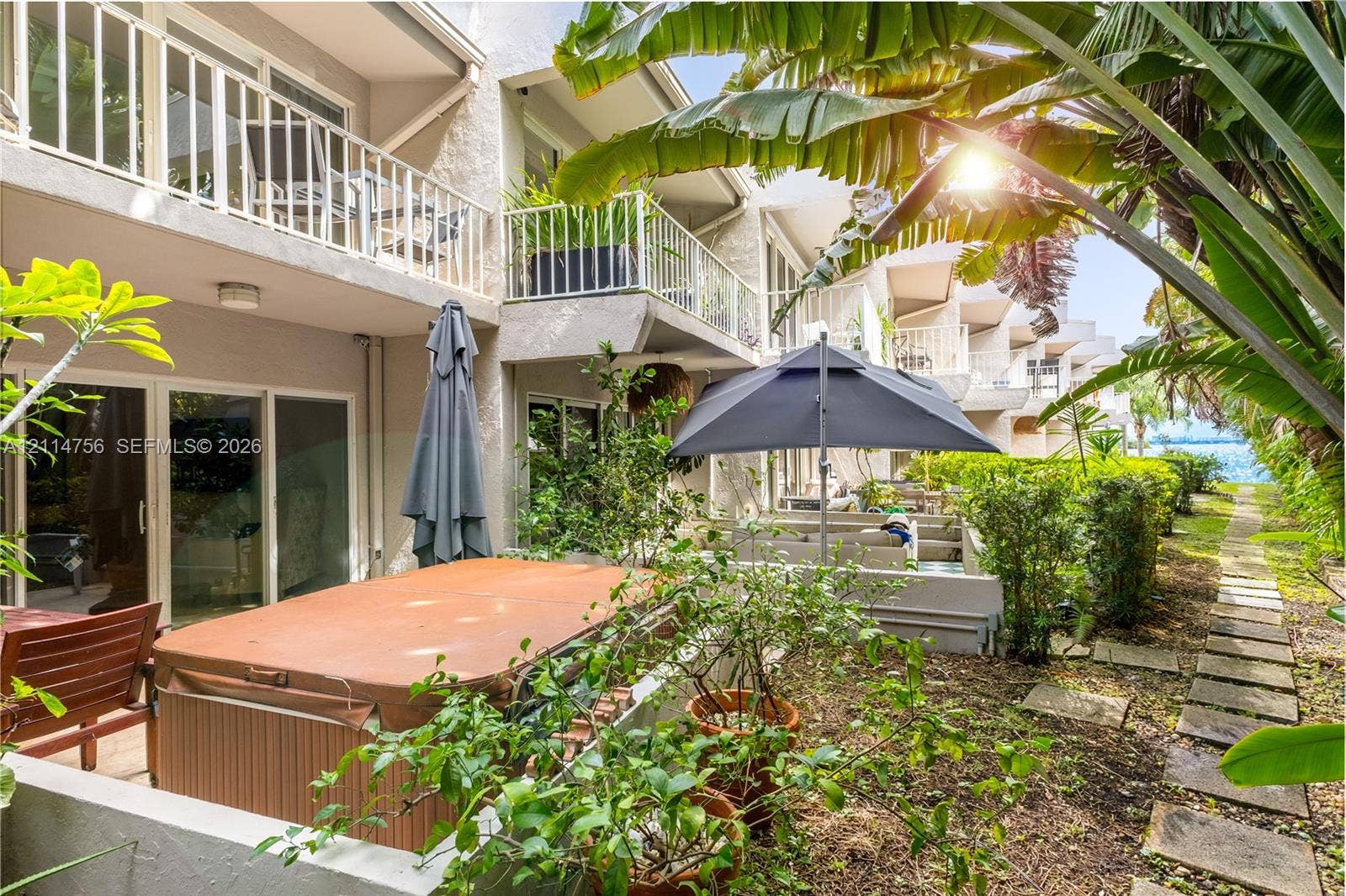 Exterior patio space featuring a hot tub, multiple levels of private balconies with white railings, and a stone paver path