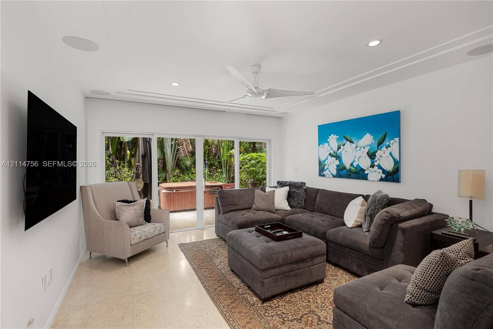 Living area featuring neutral stone flooring, crown molding, ceiling fan with integrated lighting, built-in ceiling speakers, and sliding glass doors