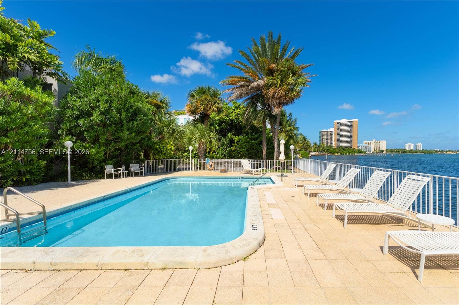Inground swimming pool with a metal perimeter fence, expansive tiled deck, and mature palm tree landscaping overlooking the water