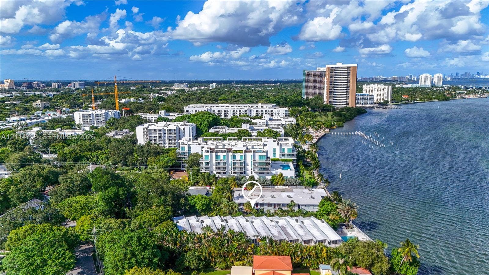 Aerial perspective of a multi-unit property featuring coastal waterfront positioning, mature landscaping, flat-roof architecture, and proximity to open water