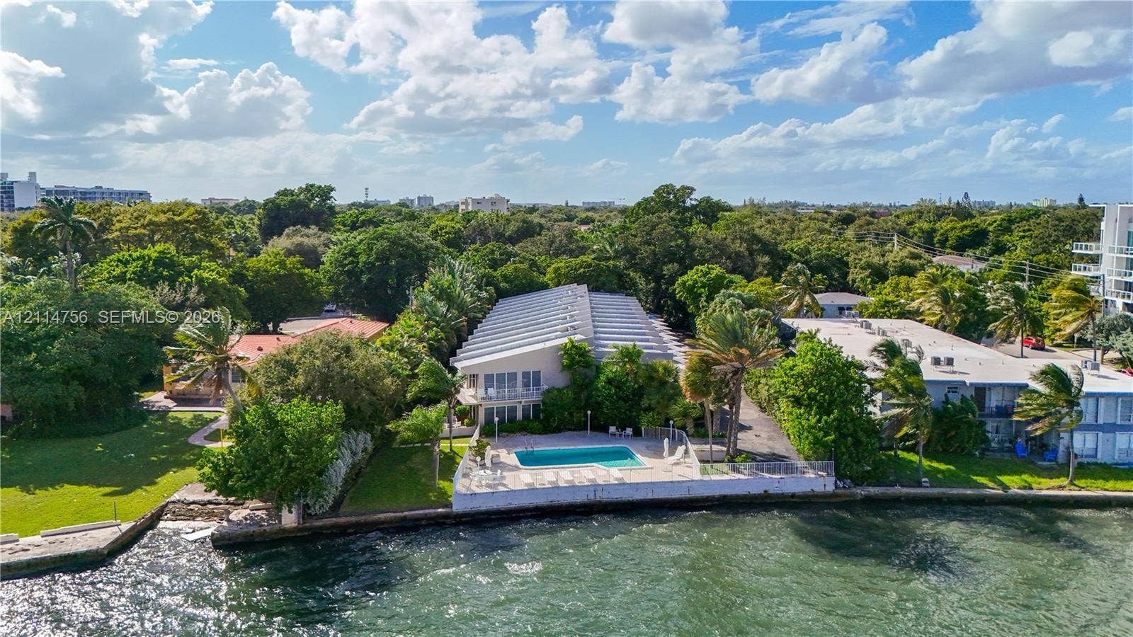 Waterfront property featuring a concrete seawall, in-ground swimming pool, paved patio, and mature landscaping