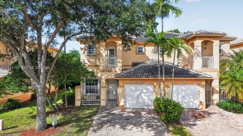 662 NW 170th Terrace, Pembroke Pines, FL 33028 Stucco exterior featuring dual-level balconies with metal railings, a tiled roof, two-car garage bays, and a decorative brick paver driveway