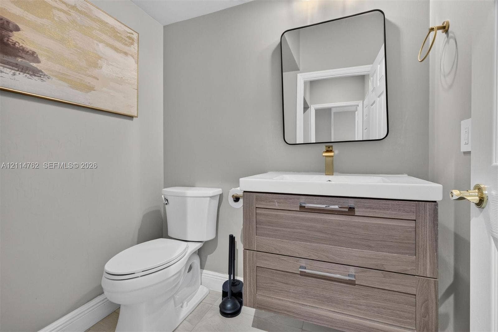 662 NW 170th Terrace, Pembroke Pines, FL 33028 Floating wood-finish vanity with an integrated white sink, gold-toned faucet, square wall-mounted mirror, and gold-toned towel ring