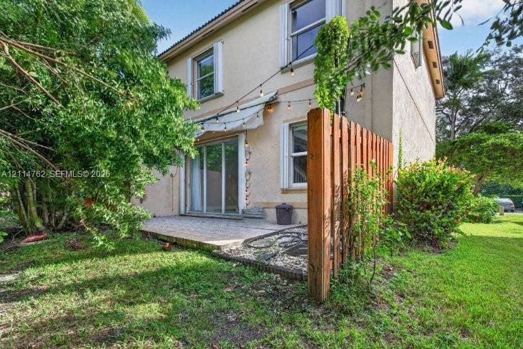 662 NW 170th Terrace, Pembroke Pines, FL 33028 Stucco exterior featuring a paved patio, retractable awning, wood privacy fencing, and sliding glass doors