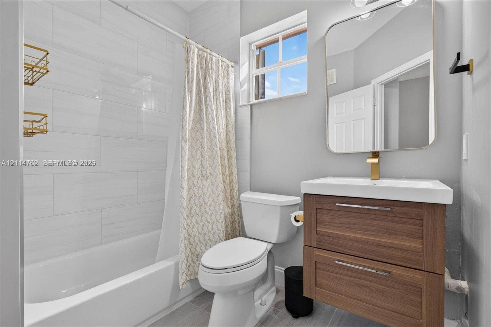 662 NW 170th Terrace, Pembroke Pines, FL 33028 Bathroom featuring a wood-finish floating vanity, rectangular vessel sink, brass-tone hardware, and a tub enclosure with horizontal wall tile