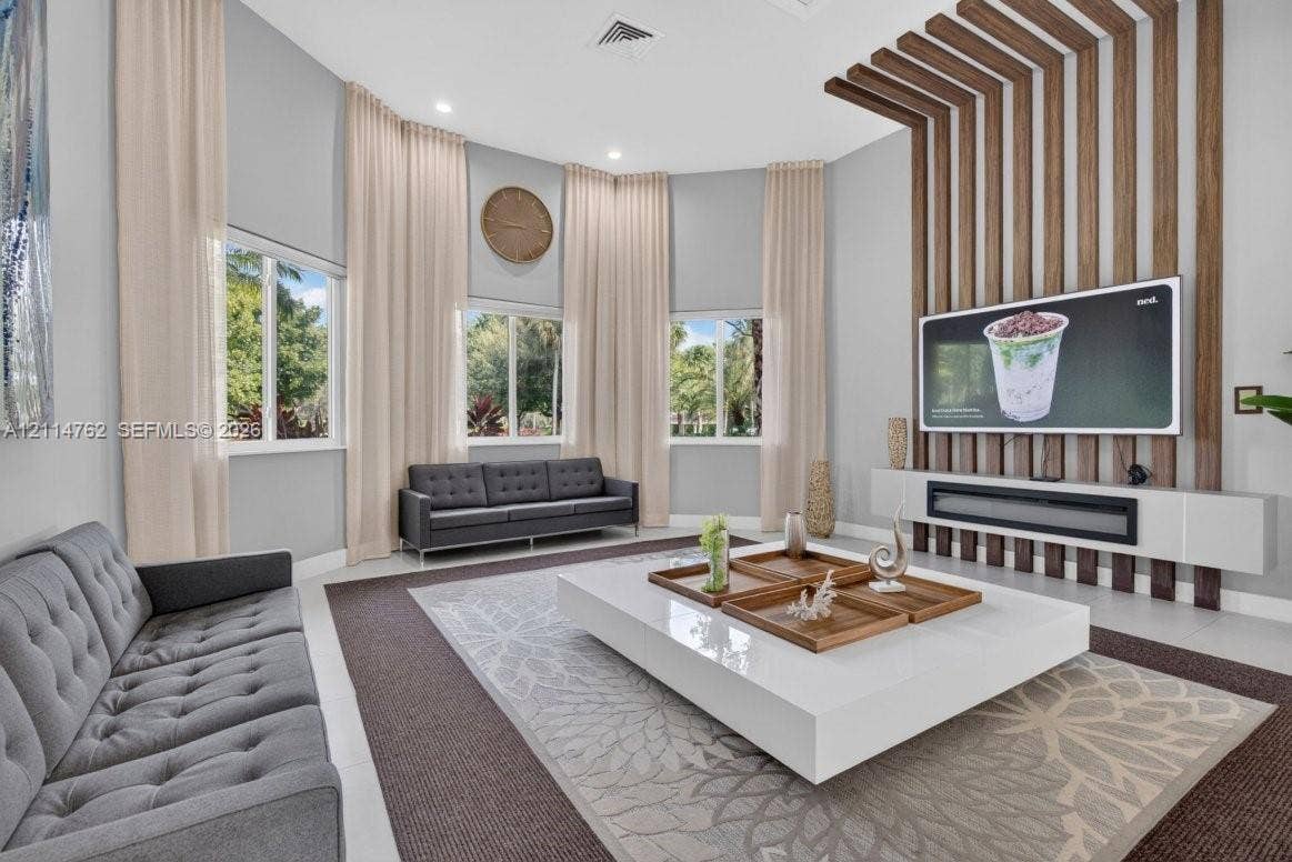 662 NW 170th Terrace, Pembroke Pines, FL 33028 Vaulted ceilings, floor-to-ceiling wooden slat accent wall, integrated horizontal linear fireplace, and large windows with extensive drapery