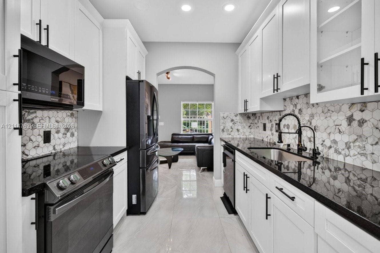 662 NW 170th Terrace, Pembroke Pines, FL 33028 Kitchen featuring white cabinetry with matte black hardware, dark stone countertops, geometric patterned tile backsplash, recessed lighting, and stainless steel appliances