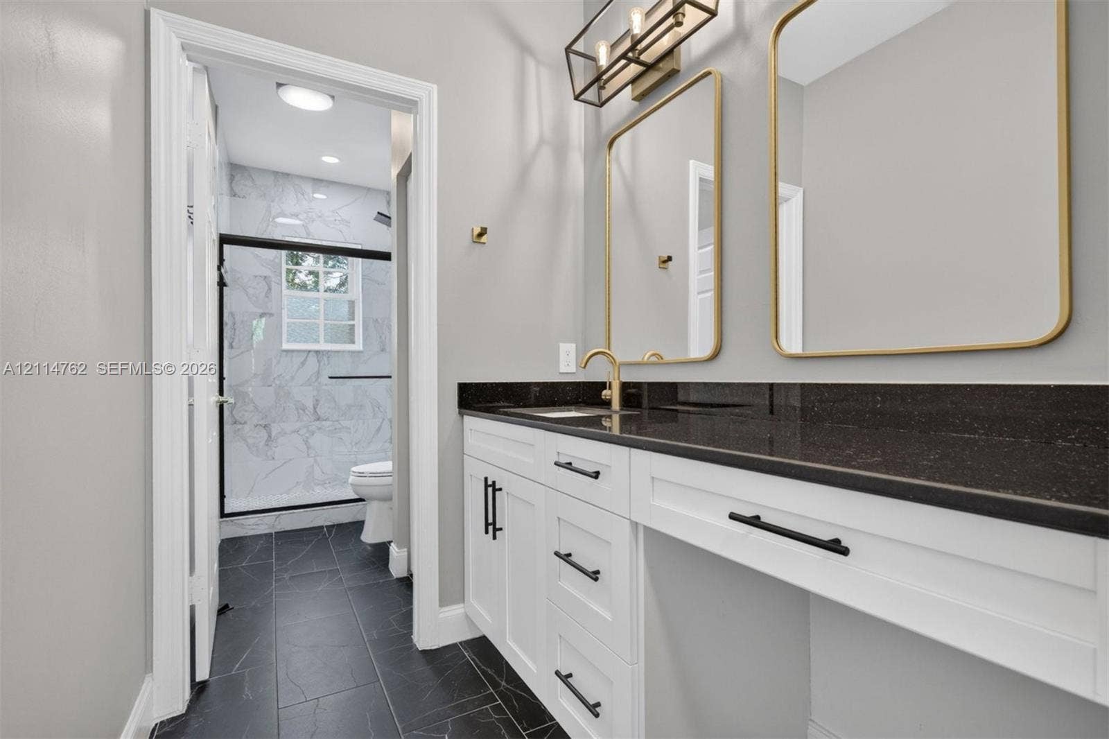 662 NW 170th Terrace, Pembroke Pines, FL 33028 White shaker cabinetry with matte black hardware, dark countertop, dual mirrors with gold-tone frames, and large-format tile flooring