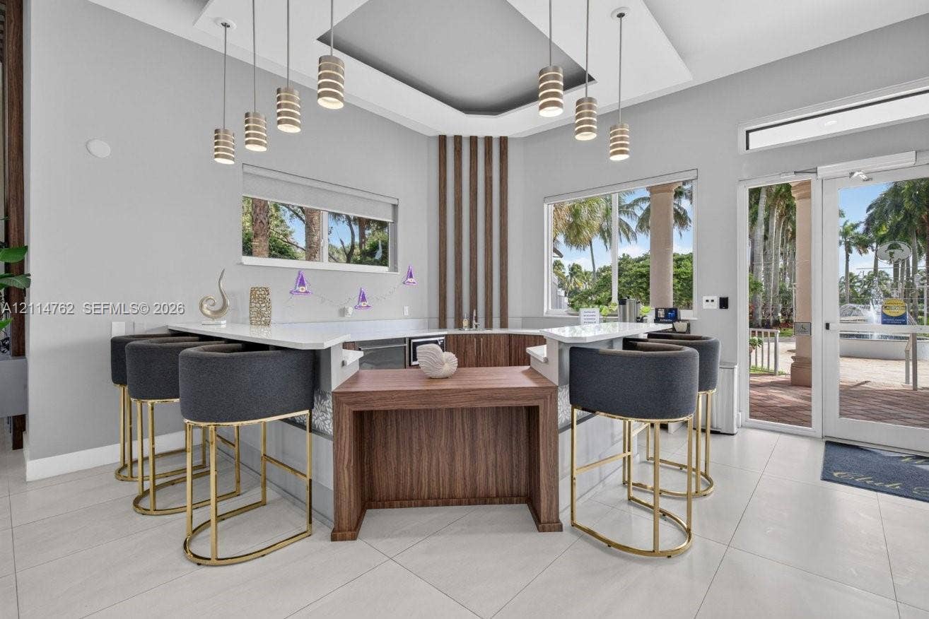 662 NW 170th Terrace, Pembroke Pines, FL 33028 Built-in wet bar featuring custom wood-finish cabinetry, stone-surface countertops, tiered multi-level workspace, and cylindrical pendant lighting suspended from a tray ceiling
