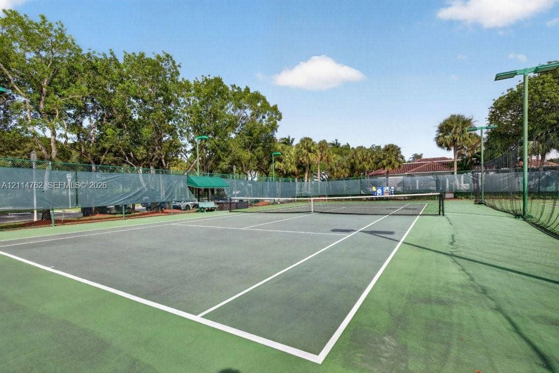 662 NW 170th Terrace, Pembroke Pines, FL 33028 Hard-surface tennis court featuring perimeter chain-link fencing, protective mesh wind screening, integrated stadium-style lighting, and surrounding mature trees