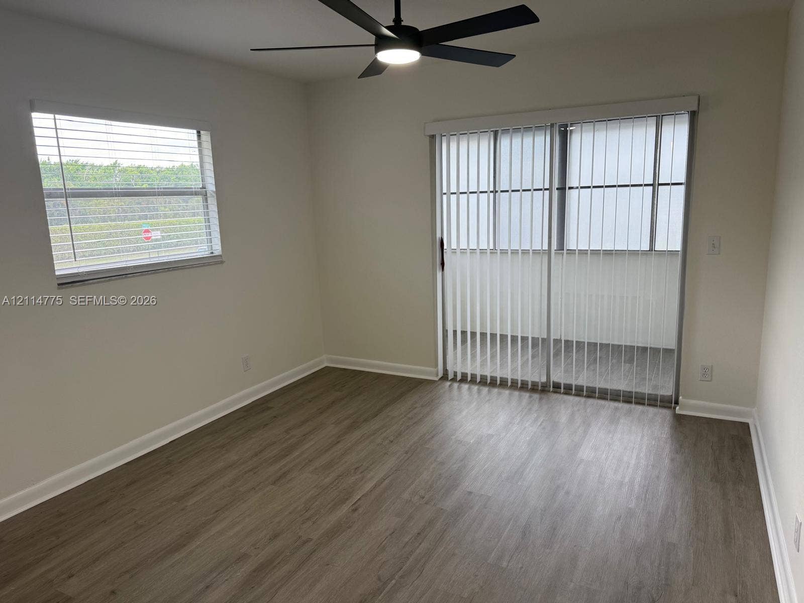 653 N Saxony N, #653, Delray Beach, FL 33446 Room featuring wood-finish flooring, a matte black ceiling fan with integrated lighting, horizontal window blinds, and sliding glass doors with vertical blinds