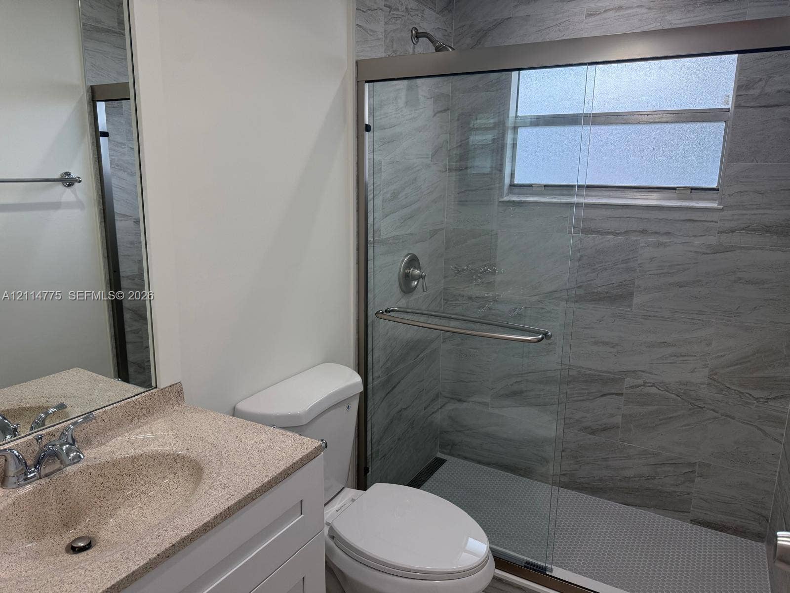 653 N Saxony N, #653, Delray Beach, FL 33446 Bathroom featuring a vanity with a neutral-toned countertop, a frameless glass-enclosed shower, floor-to-ceiling stone-patterned wall tile, and a built-in towel bar