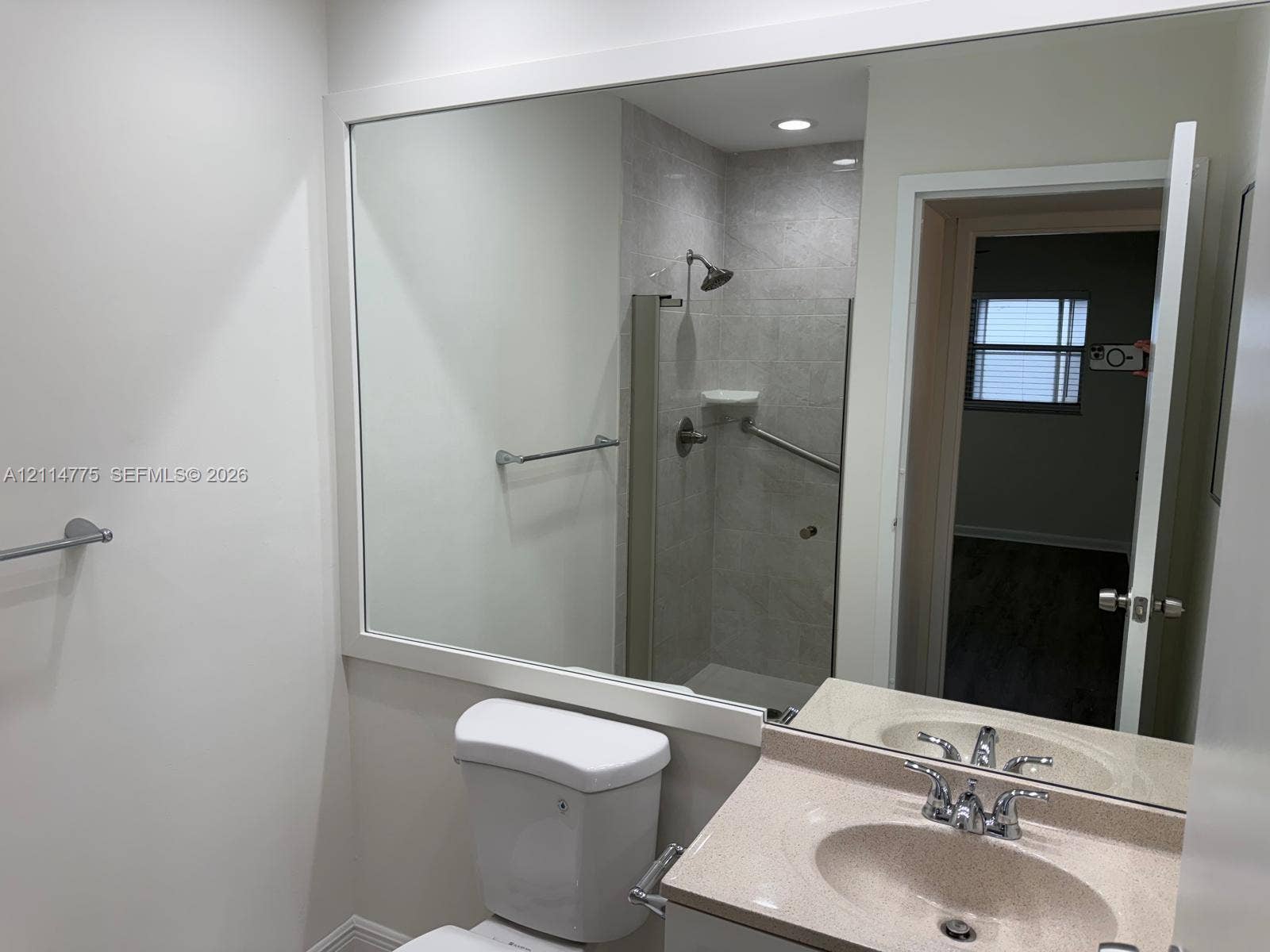 653 N Saxony N, #653, Delray Beach, FL 33446 Bathroom featuring a vanity with a solid-surface countertop, an integrated sink, a large wall-mounted mirror, and a walk-in shower with stone-finish wall tile