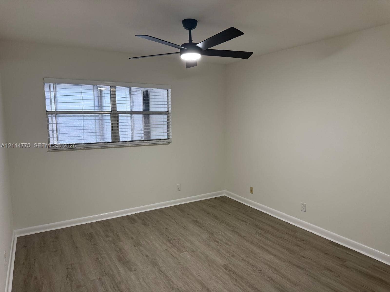 653 N Saxony N, #653, Delray Beach, FL 33446 Room featuring wood-finish flooring, a matte black ceiling fan with integrated lighting, and a multi-pane window with installed blinds