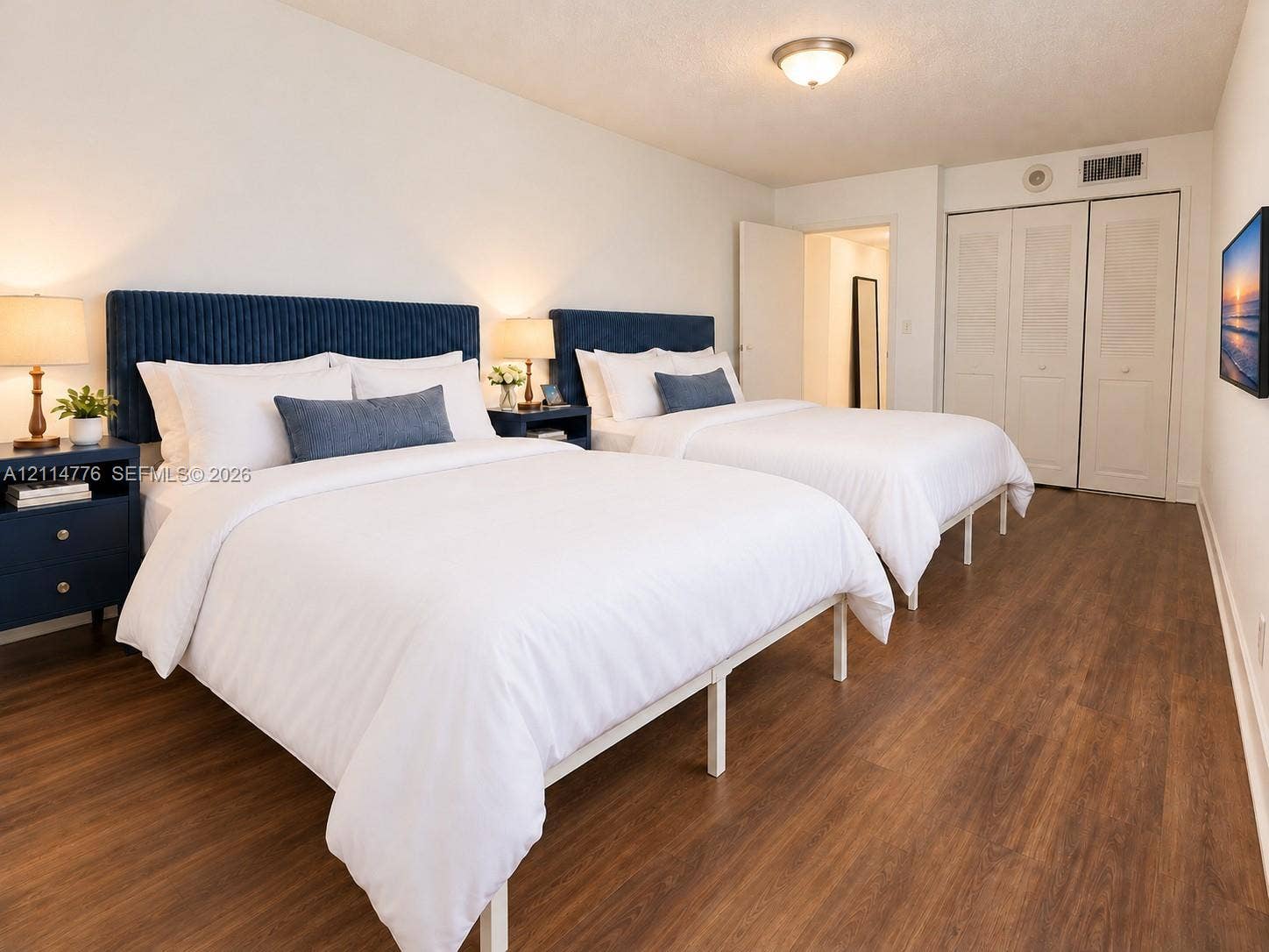 Wood-finish flooring, dual built-in closets with louvered doors, and a central flush-mount ceiling light fixture