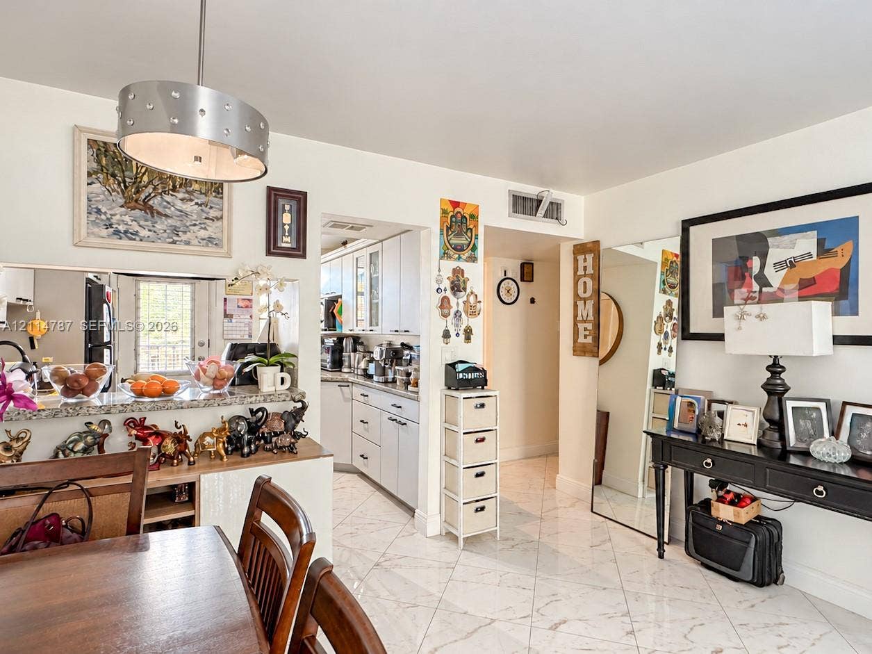 Open-concept floor plan featuring stone-topped breakfast bar, polished tile flooring, contemporary drum pendant lighting, and cabinetry with integrated glass-front doors