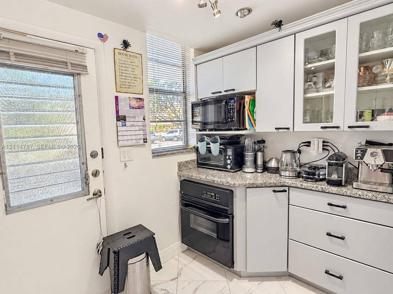 Kitchen featuring white cabinetry with glass-front uppers, speckled stone countertops, black integrated oven, built-in microwave, and tile flooring