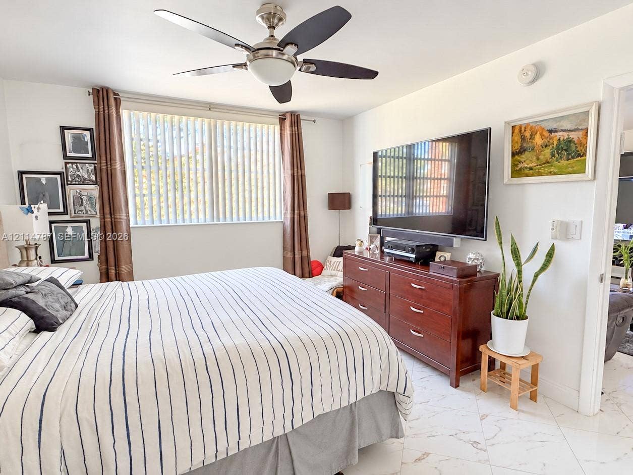 Room featuring light-toned flooring with subtle veining, ceiling fan with integrated lighting, and a window with vertical blinds