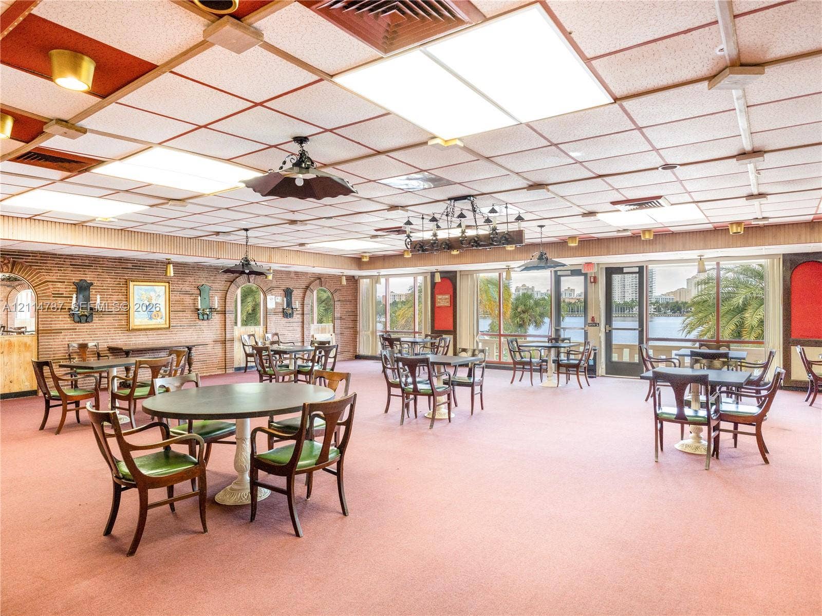 Expansive interior space featuring brick accent walls, floor-to-ceiling windows with water scenery, a drop ceiling with integrated lighting, and decorative arched wall niches