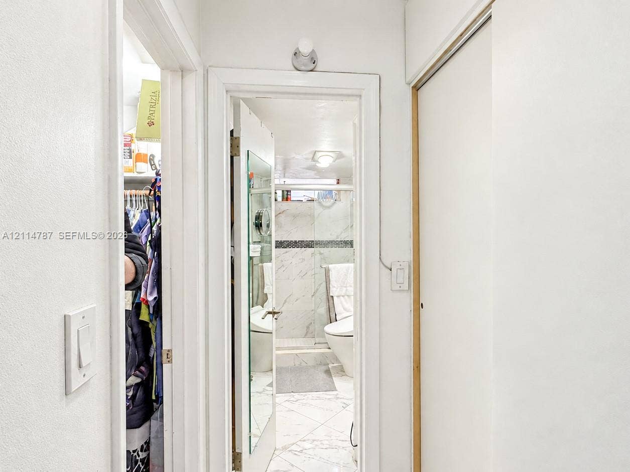 Bathroom featuring stone-finish wall and floor tiling, a glass-enclosed shower, a wall-mounted light fixture, and floor-to-ceiling closet cabinetry