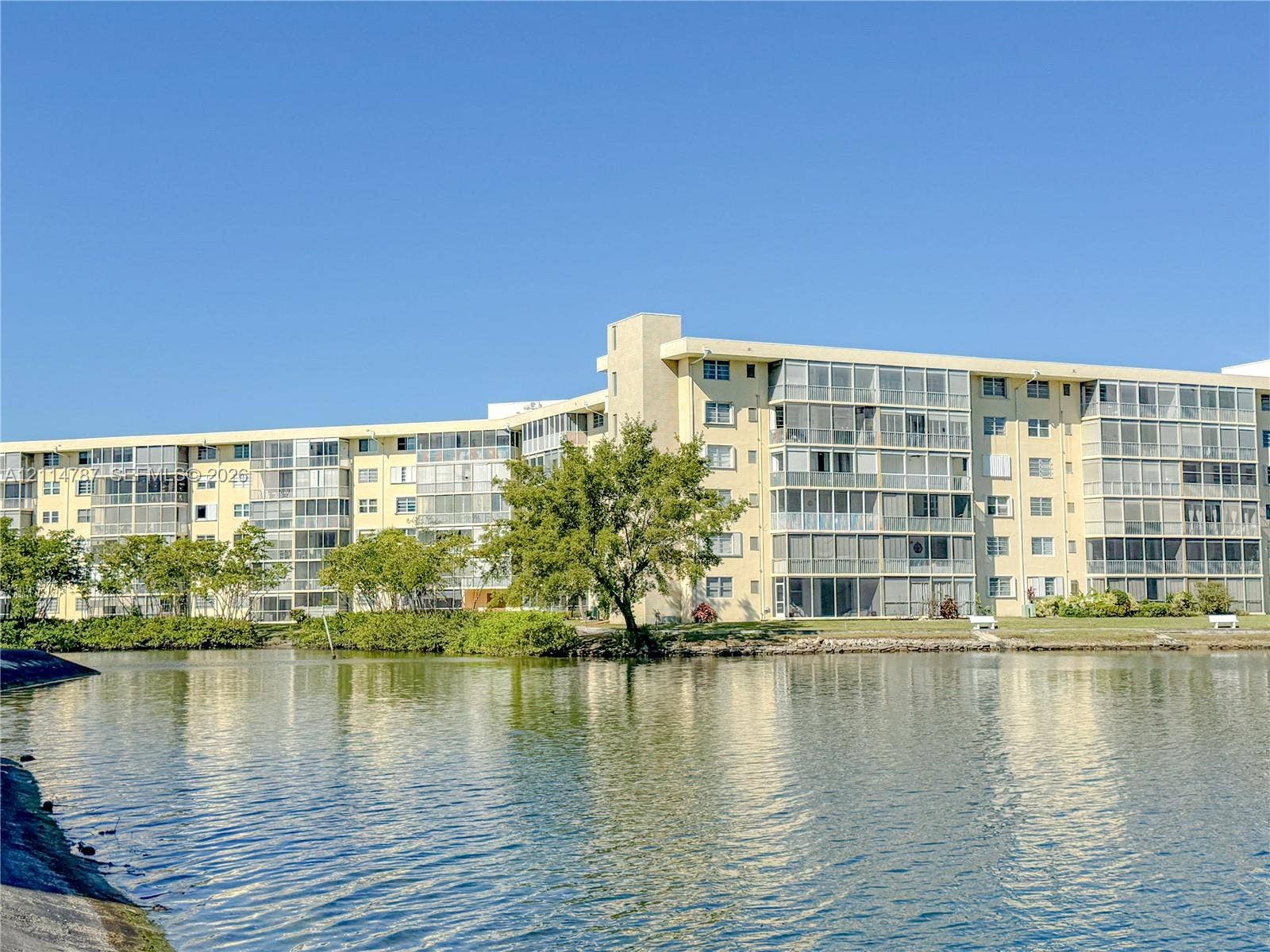 Multi-story residential building featuring enclosed balconies, concrete construction, and exterior landscaping, positioned along a waterfront