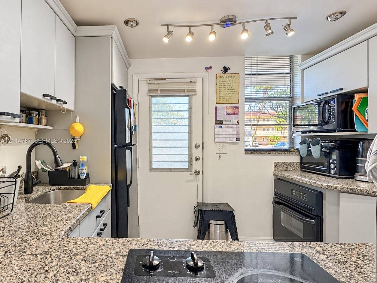 Kitchen featuring speckled stone countertops, shaker-style cabinetry, a built-in oven, a black gooseneck faucet, and multi-light track lighting