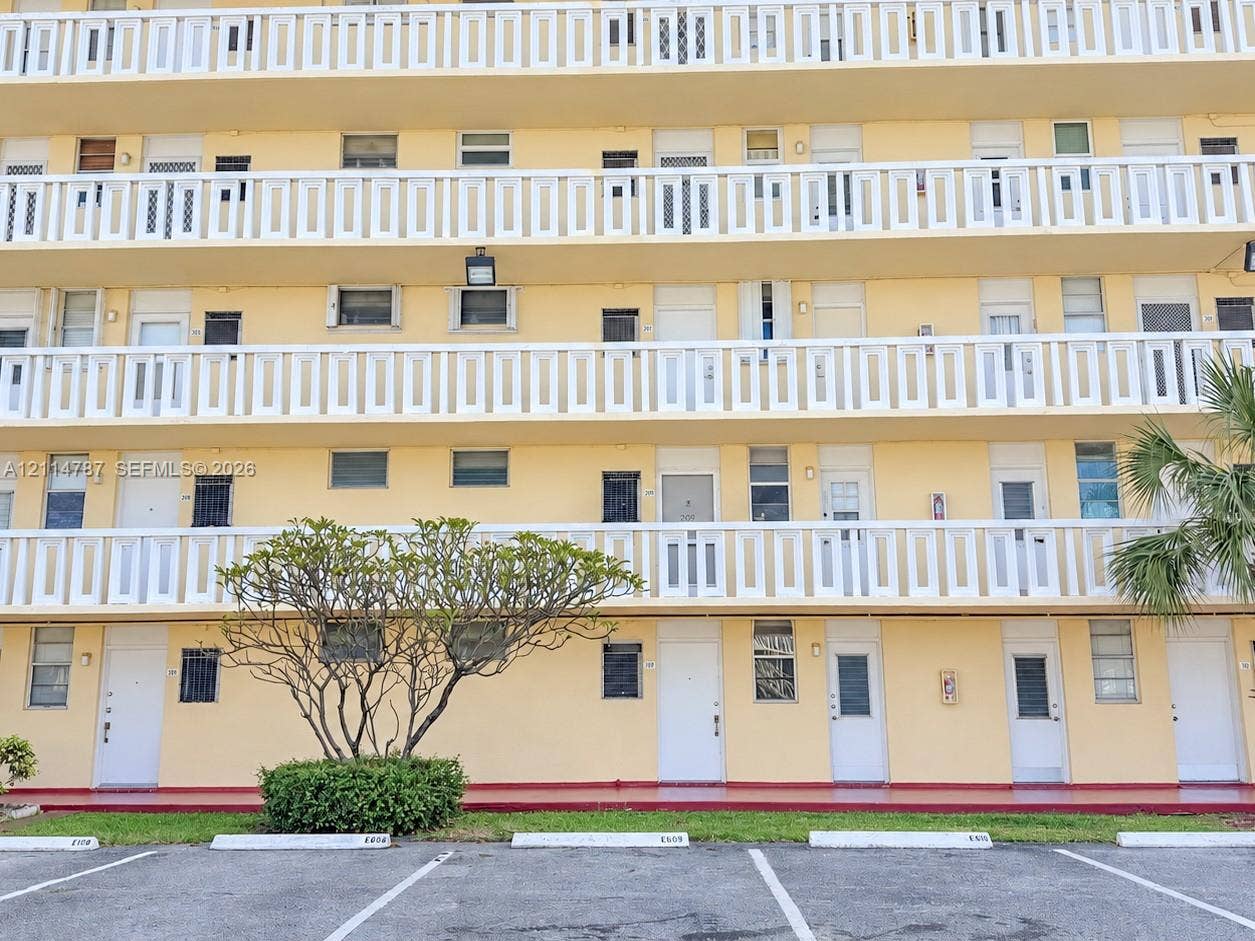 Multi-story exterior featuring continuous white balcony railings, uniform entry doors, and ground-level parking spaces