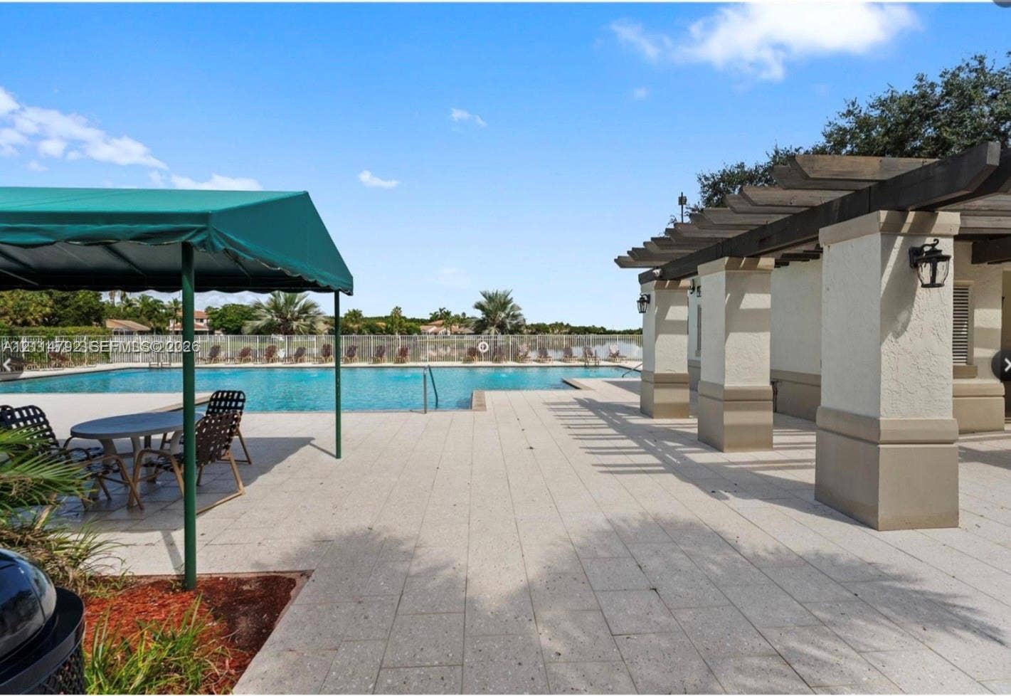 932 Falling Water Road, Weston, Weston, FL 33326 Outdoor pool area featuring a stone-paver patio, wood-beam pergola, green canvas awning, and metal perimeter fencing