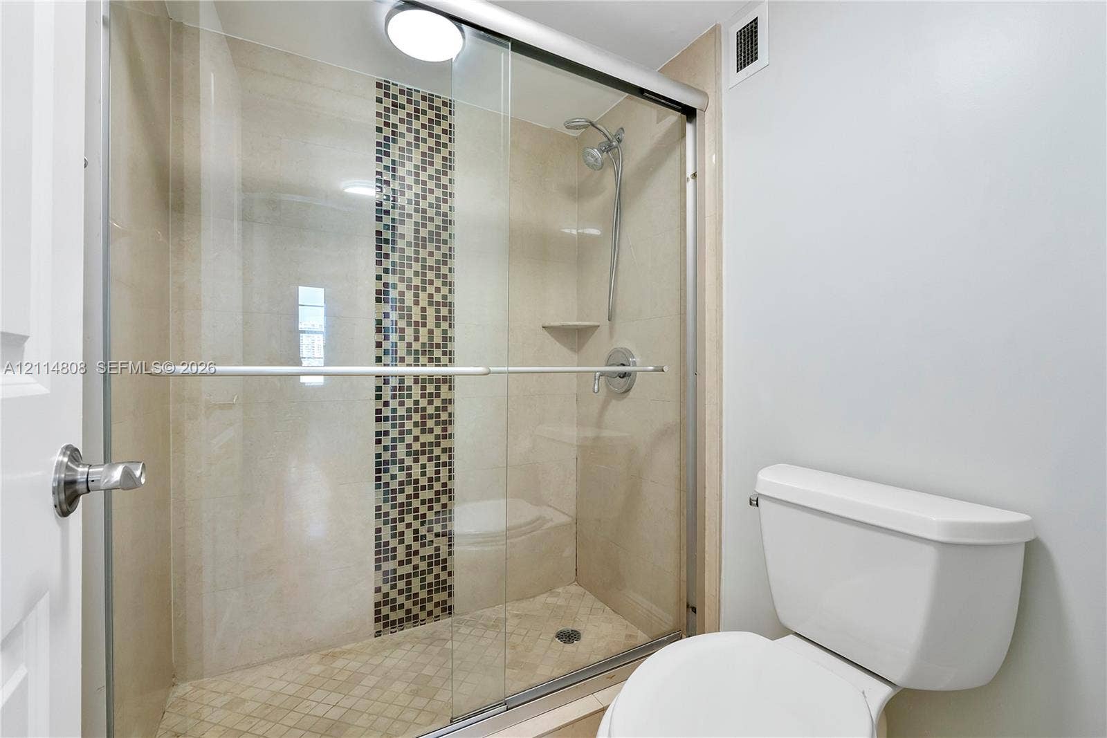 1000 S Ocean Boulevard, #16P, Pompano Beach, Pompano Beach, FL 33062 Walk-in shower featuring a sliding glass enclosure, decorative vertical tile accent, built-in corner shelving, integrated shower head with handheld attachment, and tile flooring