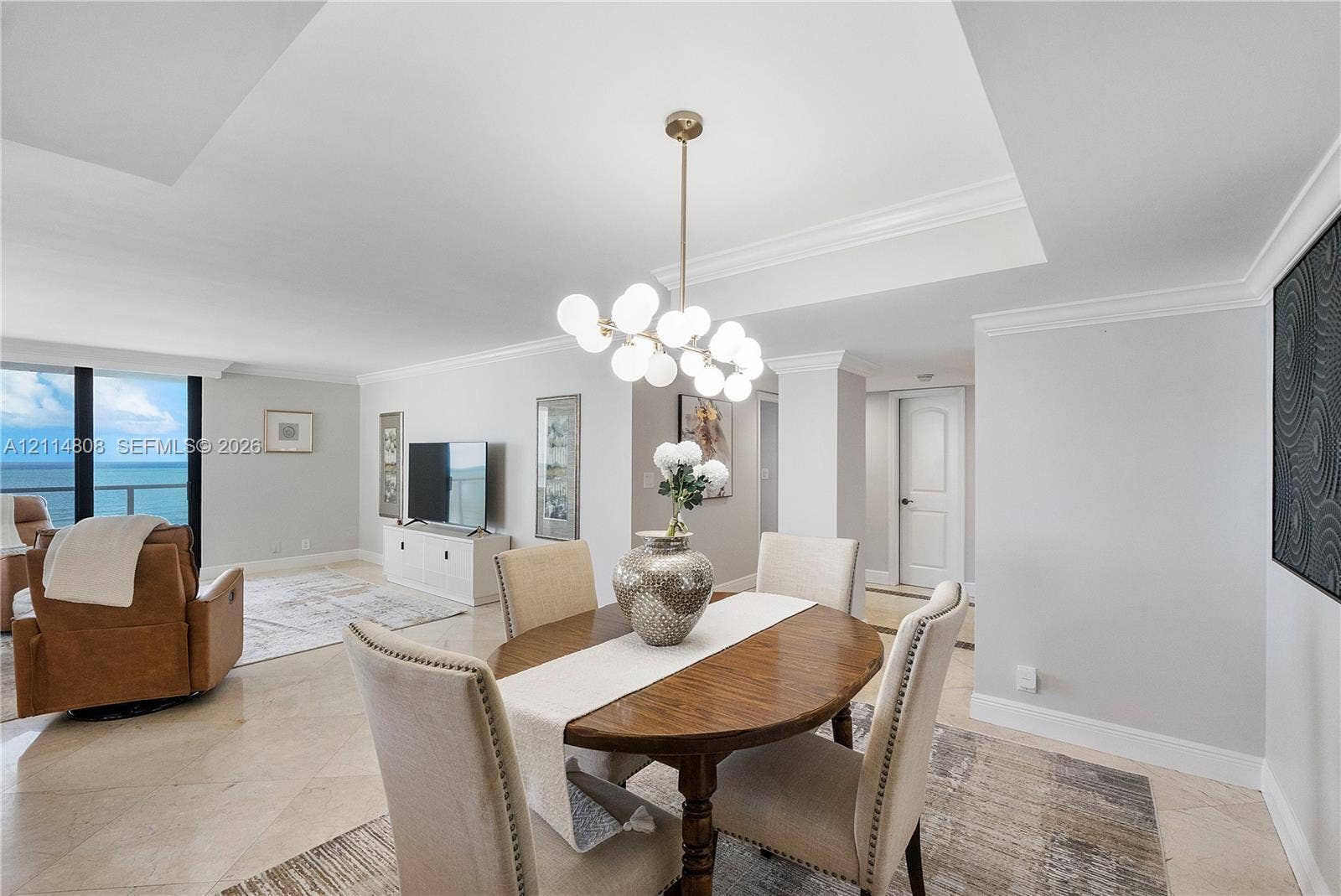 1000 S Ocean Boulevard, #16P, Pompano Beach, Pompano Beach, FL 33062 Open-concept interior featuring light-toned stone tile flooring, tray ceilings with crown molding, a multi-globe pendant light fixture, and floor-to-ceiling windows with ocean scenery
