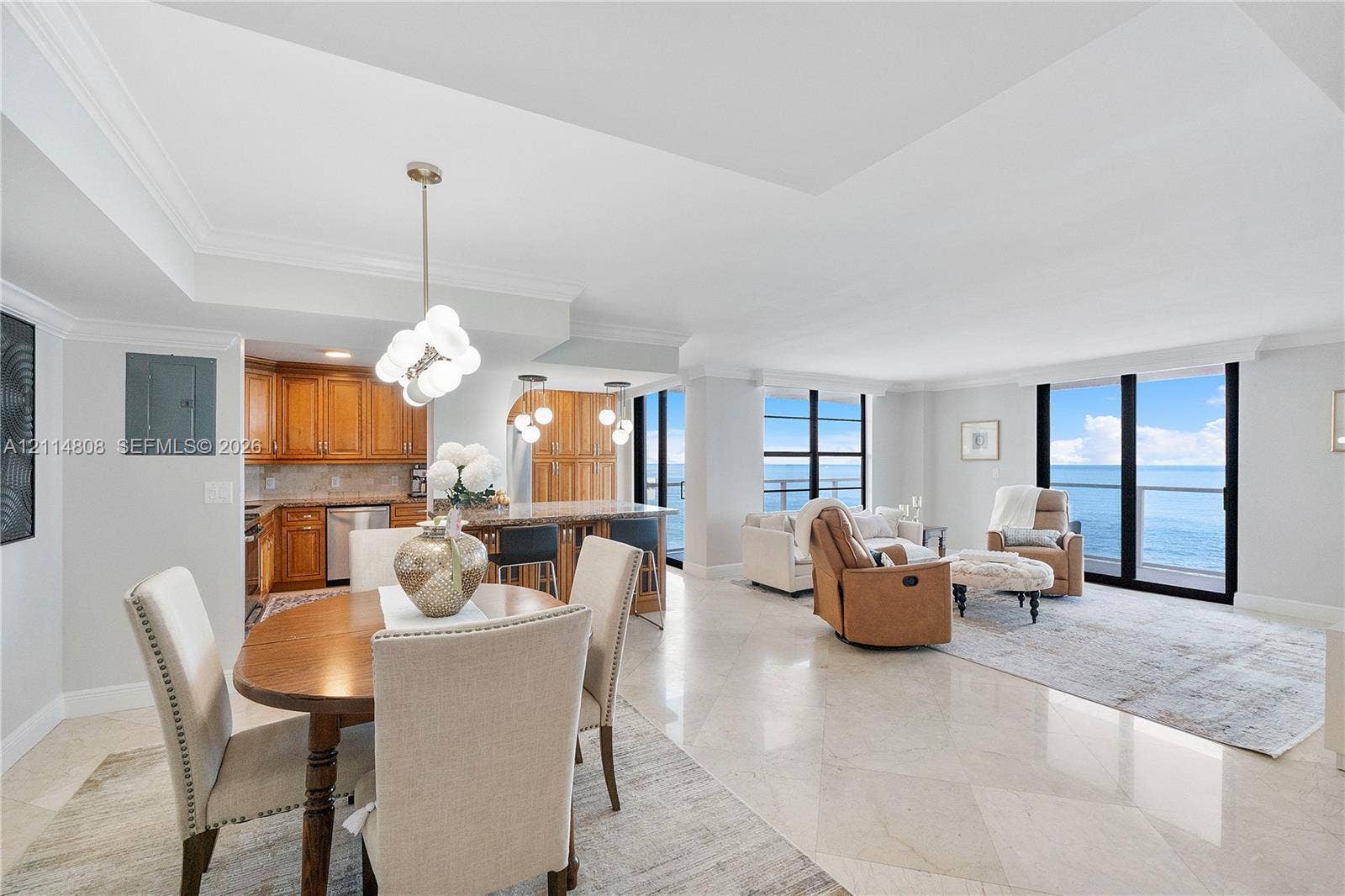 1000 S Ocean Boulevard, #16P, Pompano Beach, Pompano Beach, FL 33062 Open-concept interior featuring tray ceilings, natural stone flooring, floor-to-ceiling windows with water backdrop, and custom cabinetry with integrated lighting