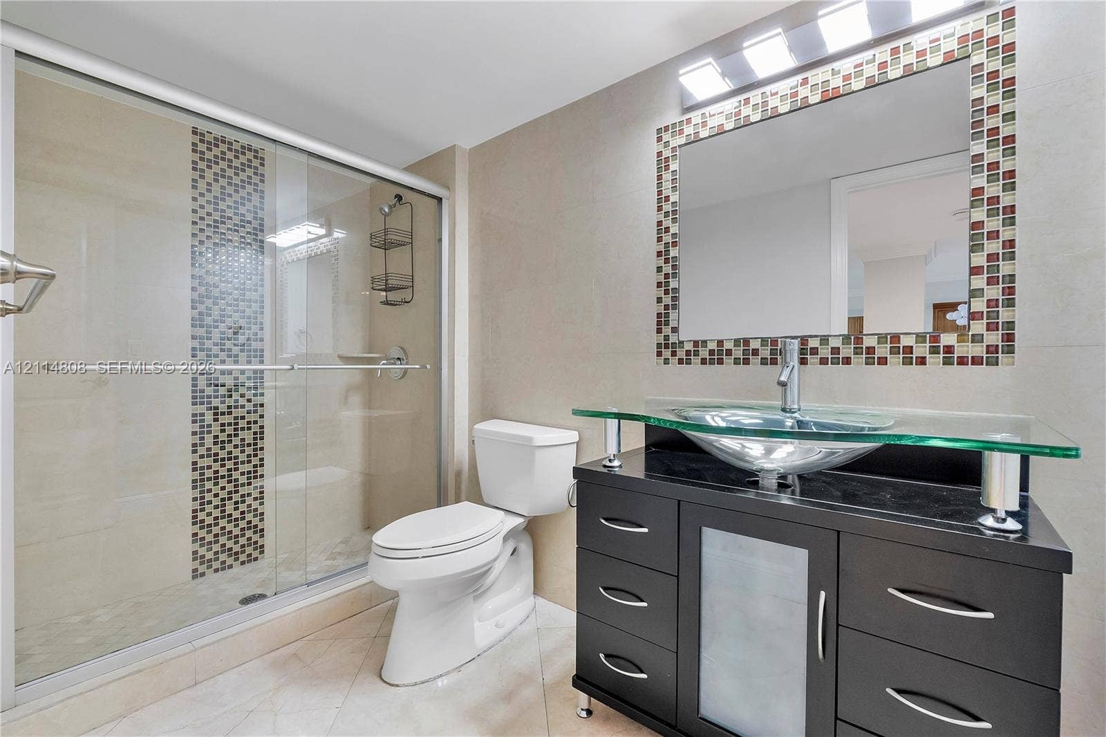 1000 S Ocean Boulevard, #16P, Pompano Beach, Pompano Beach, FL 33062 Modern vanity featuring a black finish, glass countertop, and vessel sink, paired with a glass-enclosed shower with mosaic tile accents, matching mosaic tile framed mirror, and light-toned tile flooring