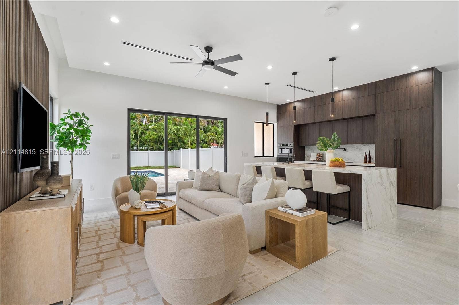 Open-concept interior featuring wood-finish cabinetry, a waterfall-edge kitchen island, stone-surfaced countertops, sliding glass doors, and light-toned tile flooring