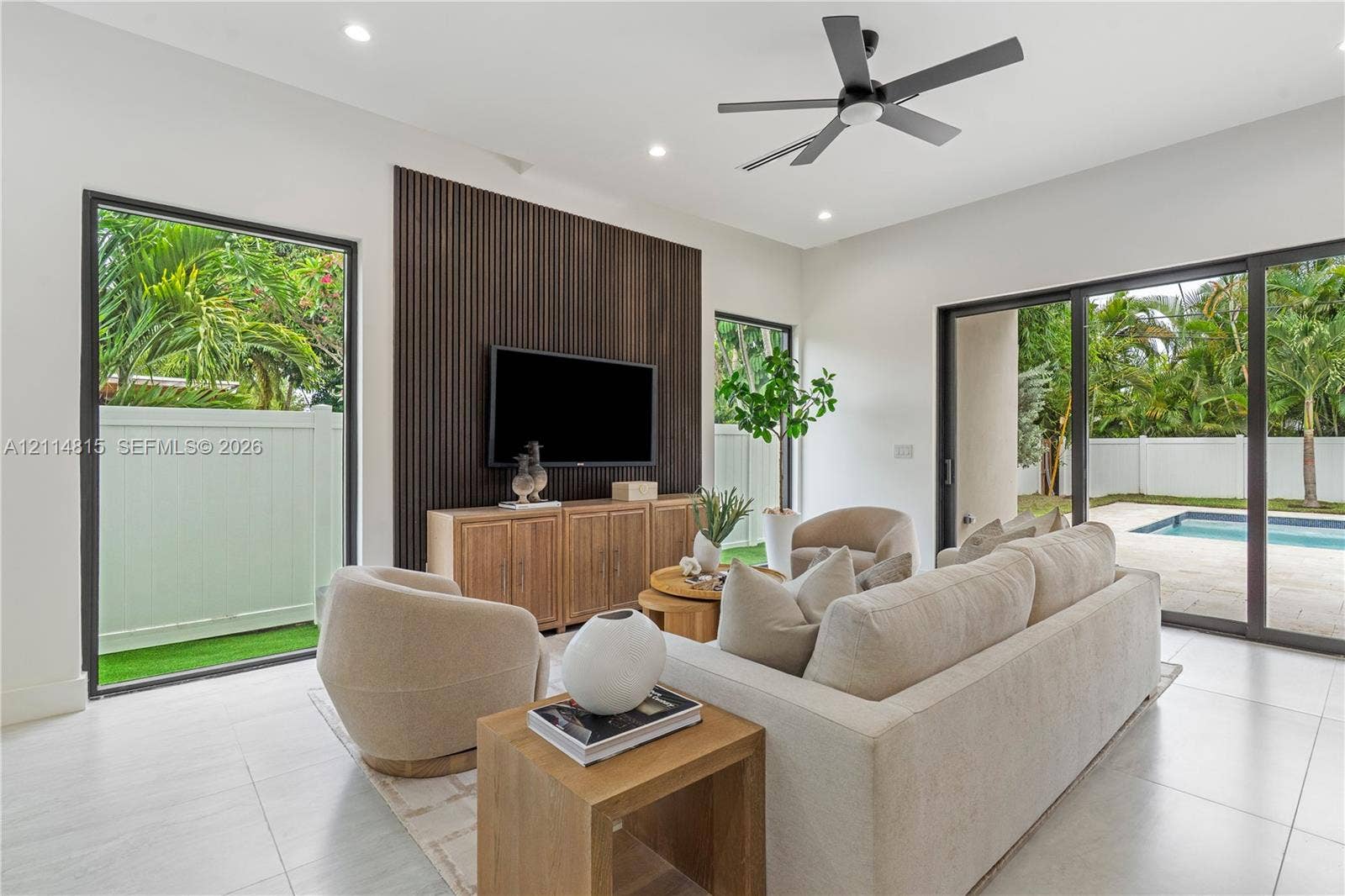 Living area featuring large-format tile flooring, a dark-toned vertical slat accent wall, recessed lighting, a modern ceiling fan, and sliding glass doors with direct access to the exterior pool area
