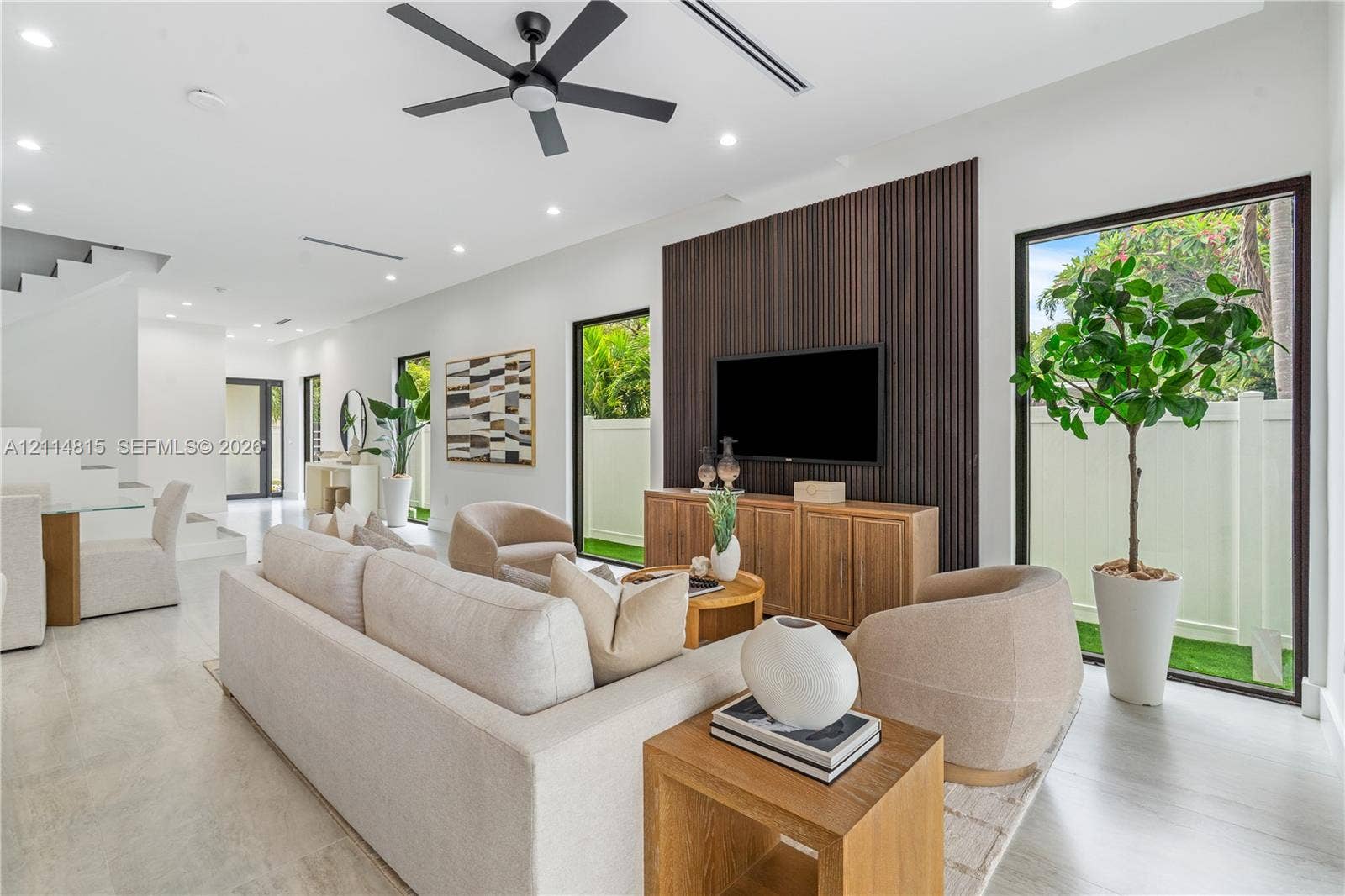 Open-concept space featuring large-format tile flooring, a floor-to-ceiling dark wood-slat accent wall, recessed lighting, a modern ceiling fan, and expansive glass doors