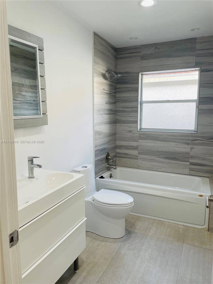 1952 Water Ridge Drive, #1952, Weston, Weston, FL 33326 Modern bathroom featuring a white floating vanity with a vessel sink, dual-flush toilet, built-in bathtub with a shower fixture, and grey-toned tile surround